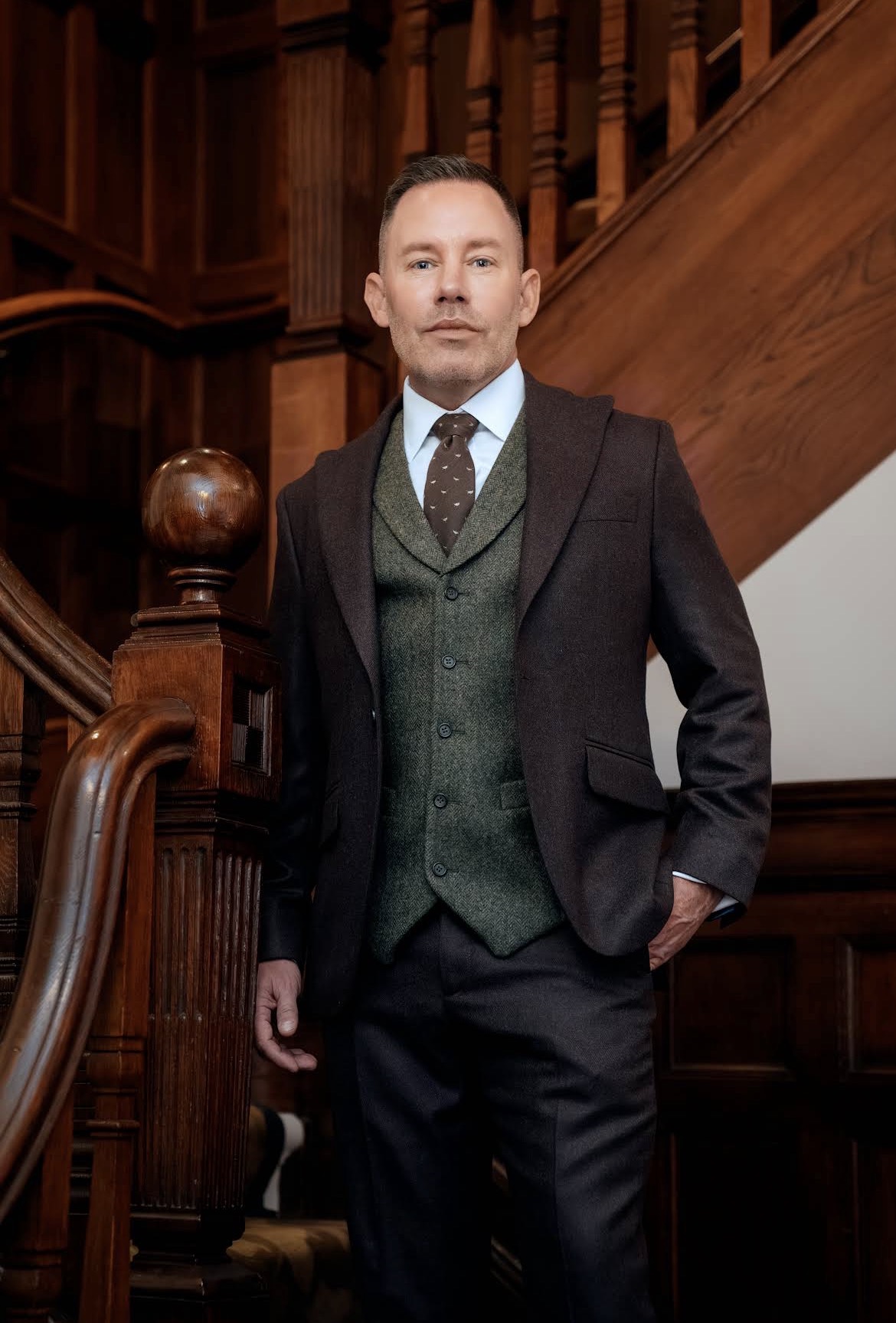 Client in a tailored tweed three-piece suit on a wooden staircase