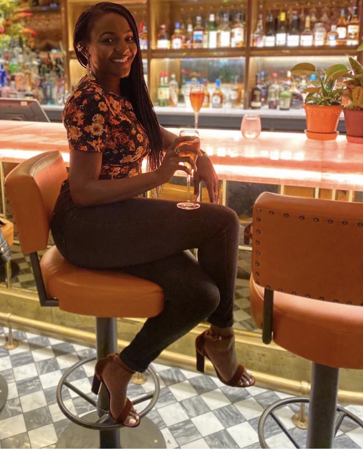 A client in a floral top and jeans seated on a bar stool with an aperitif