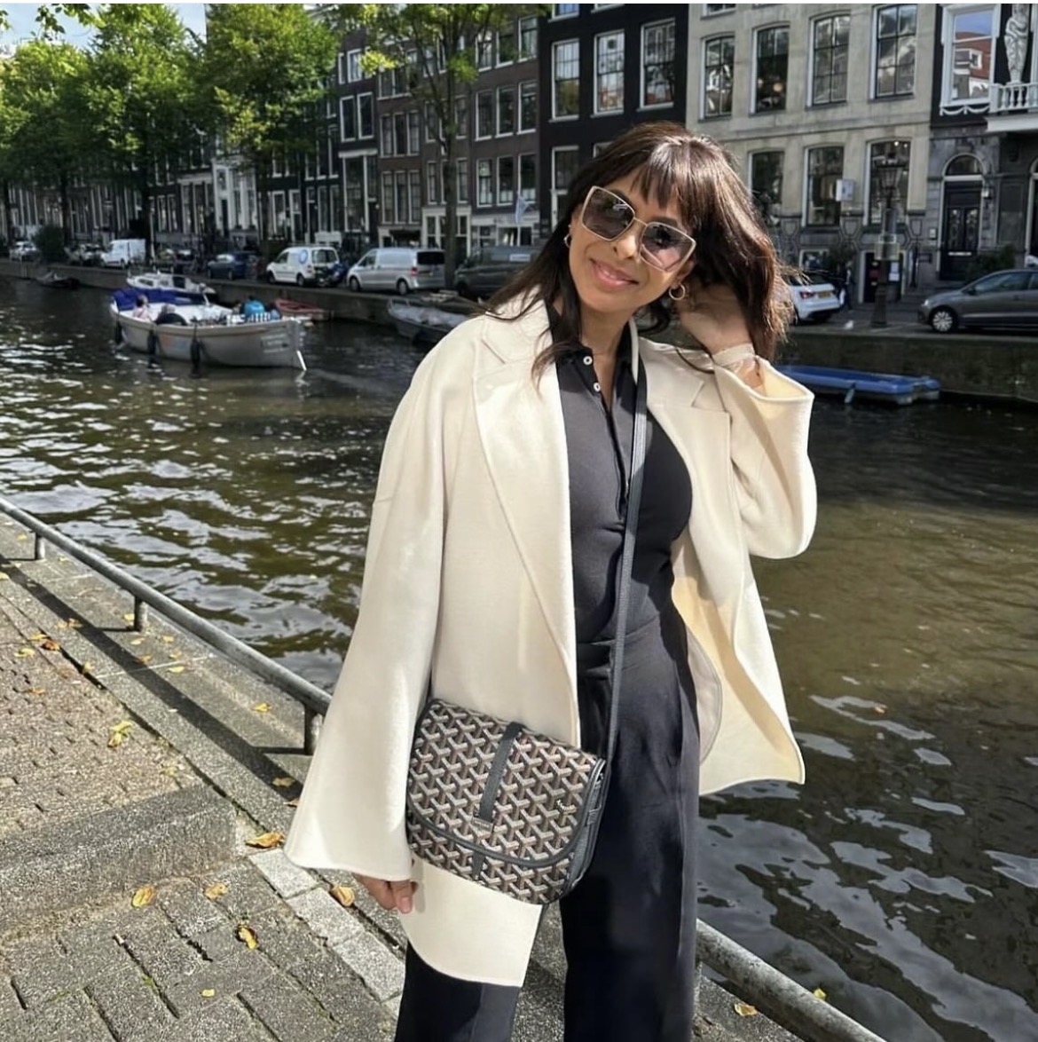 A client in a cream coat and patterned crossbody bag beside a canal